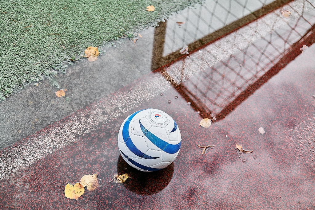 Ein Rasselball liegt in einer Pfütze mit Herbstlaub am Tor. In der Wasserspiegelung sieht man den Torrahmen