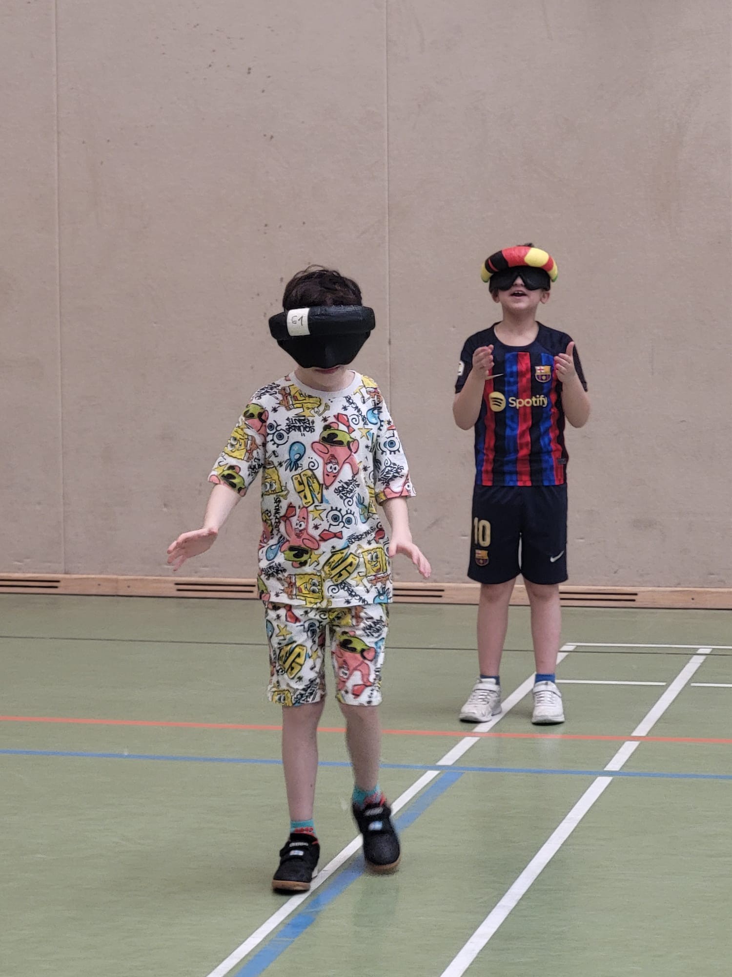 Zwei Schüler tragen Dunkelbrillen und üben Paarübungen in der Sporthalle aus