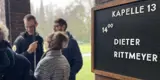 Schild mit Aufschrift "Kapelle 13 Dieter Rittmeyer 14 Uhr". Dahinter ein paar Teammitglieder