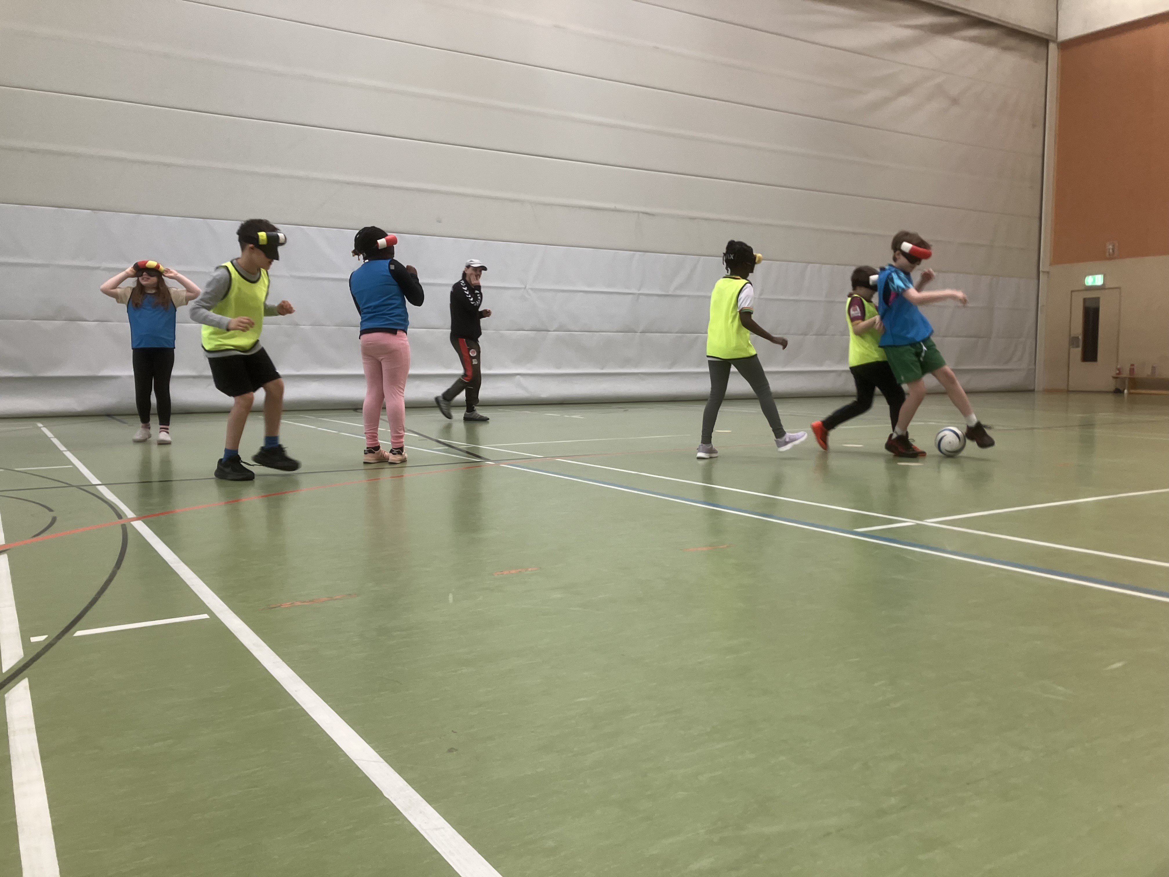 In einer Sporthalle spielen Kinder mit Dunkelbrillen Fußball